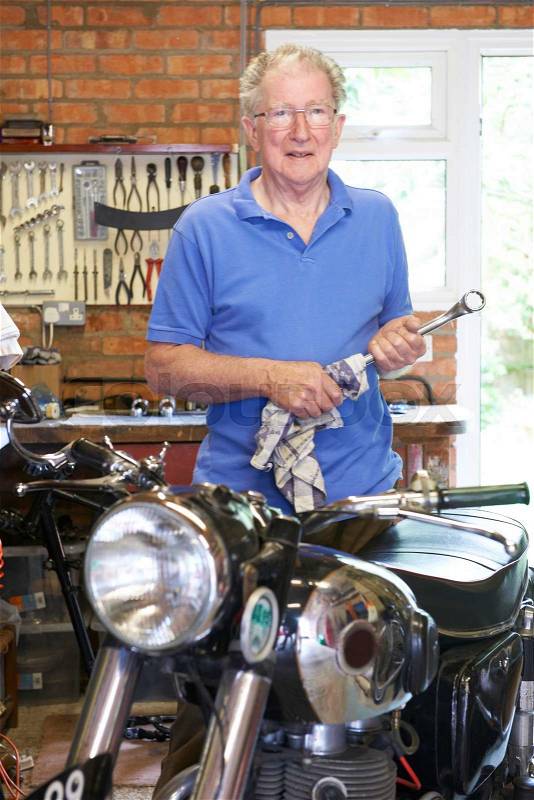 Senior Man Restoring Vintage Motorcycle In Garage, stock photo