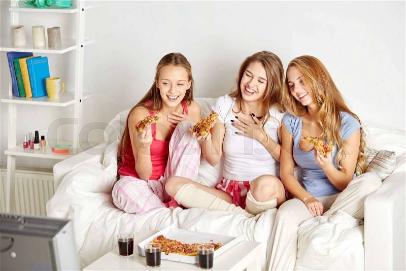 Friendship, people, pajama party, entertainment and junk food concept - happy friends or teenage girls eating pizza and watching movie or tv series at home, stock photo