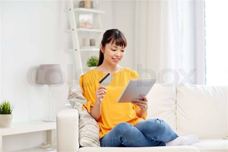 People, internet bank, online shopping, technology and e-money concept - happy asian young woman sitting on sofa with tablet pc computer and credit card at home, stock photo