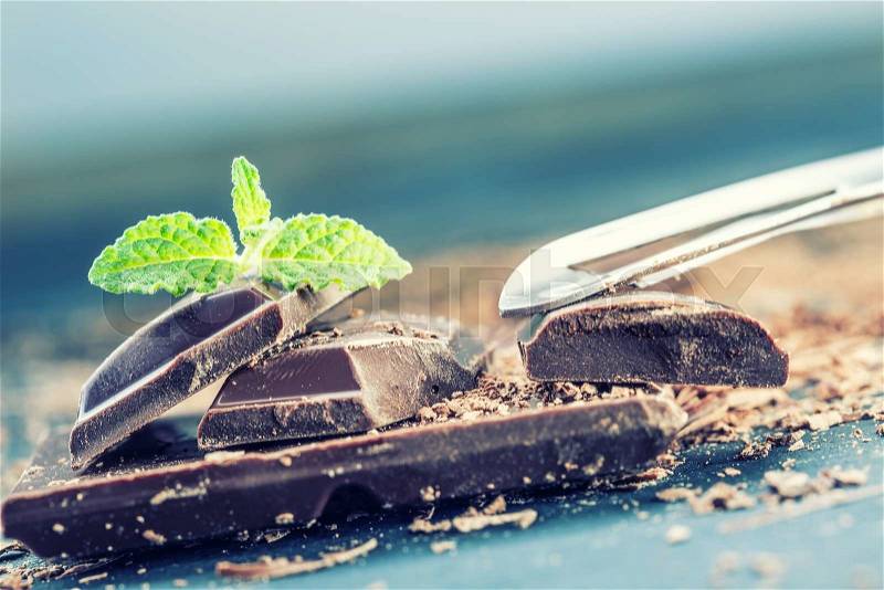Chocolate. Black chocolate. A few cubes of black chocolate with mint leaves. Chocolate slabs spilled from grated chockolate powder, stock photo