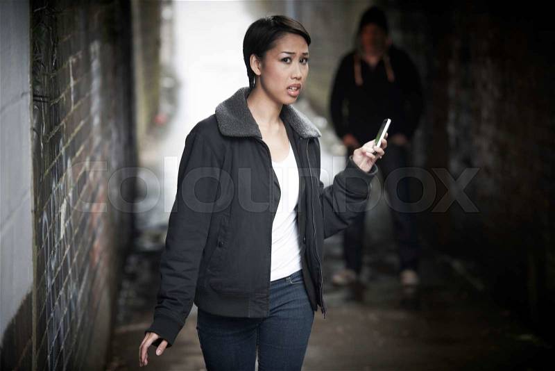 Woman Woman Walking Along City Street With Menacing Figure In Shadows, stock photo
