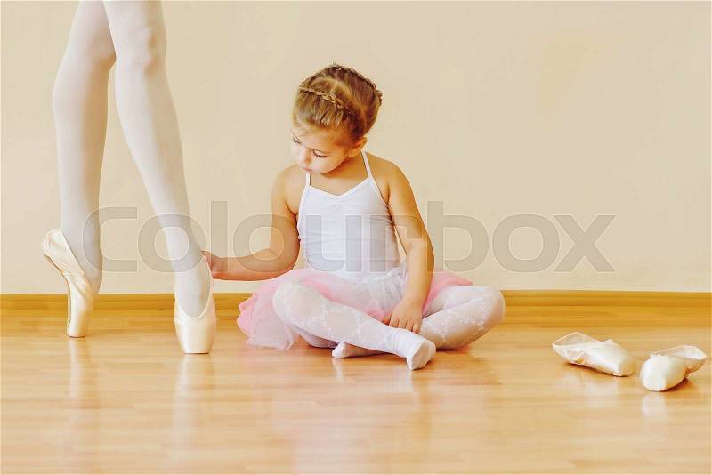 Little girl looking on feet of trainer in ballet school, stock photo