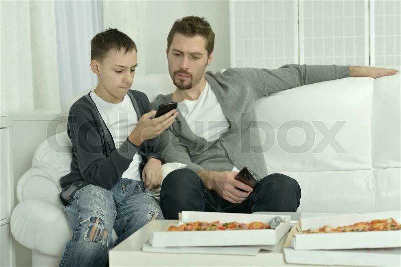 Portrait of father and son with pizza and smartphone at home, stock photo