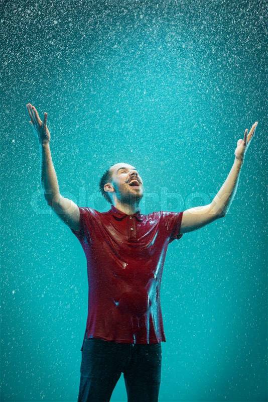 The portrait of young man in the rain. The man screaming on a turquoise background, stock photo