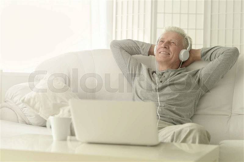 Portrait of senior man in headphones at home with laptop, stock photo