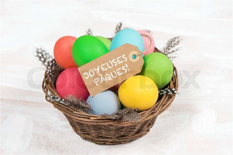 Easter eggs in basket with feather decoration. Happy Easter - JOYEUSES PÀQUES! french text, stock photo