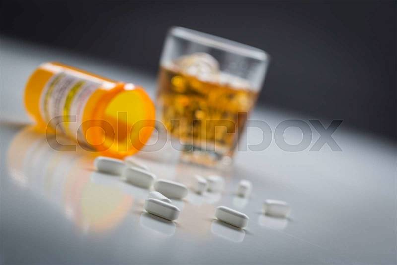 Several Prescription Drugs Spilled From Fallen Bottle Near Glass of Alcohol, stock photo