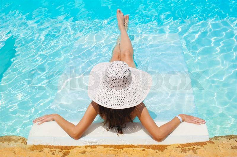 Beautiful woman white hat and bikini lying in a pool, stock photo