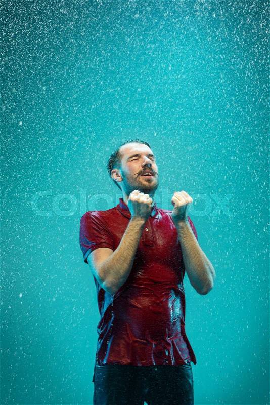 The portrait of young man in the rain. The man standing on a turquoise background, stock photo