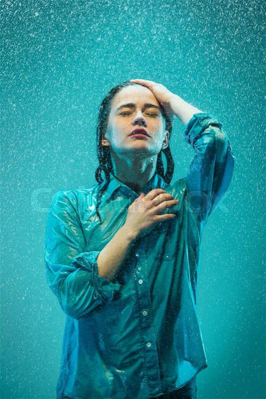 The portrait of young beautiful woman in the rain. The girl standing on a turquoise background, stock photo