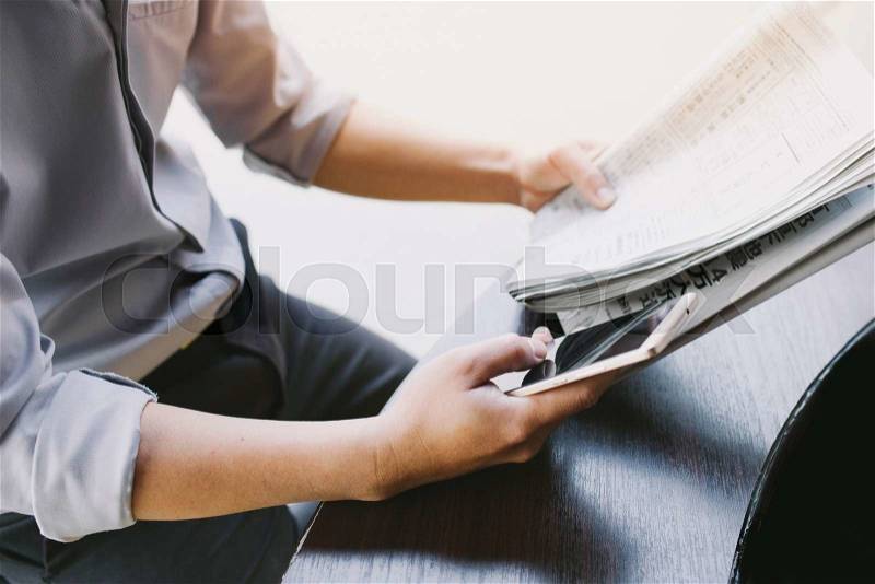 Man\'s hands holding newspaper and using smartphone for online , stock photo
