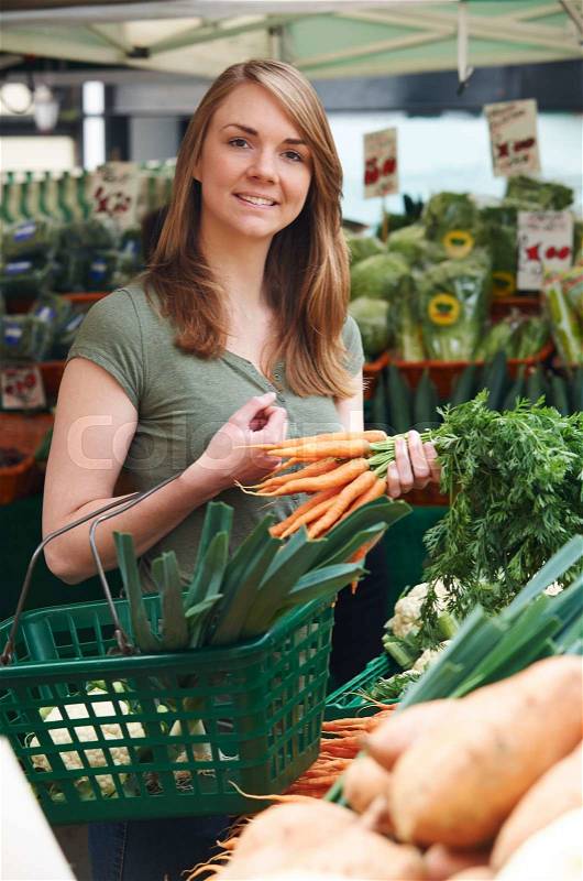 Woman Buying Carrots At Vegetable Stall In Market, stock photo