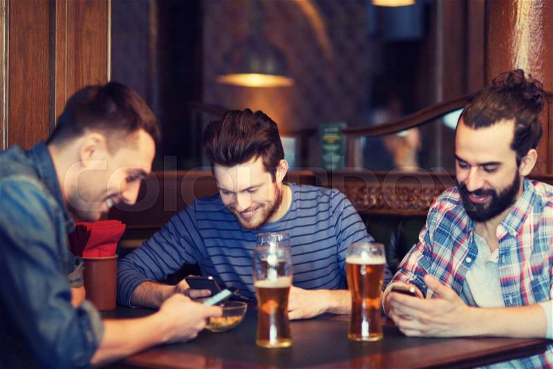 People, men, leisure, friendship and technology concept - happy male friends with smartphones drinking beer at bar or pub, stock photo