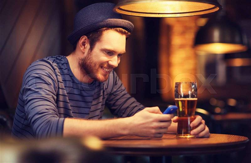 People and technology concept - happy man with smartphone drinking beer and reading message at bar or pub, stock photo
