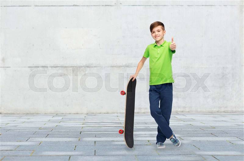 Childhood, leisure, school and people concept - happy smiling boy with skateboard showing thumbs up over concrete gray wall on city street background, stock photo
