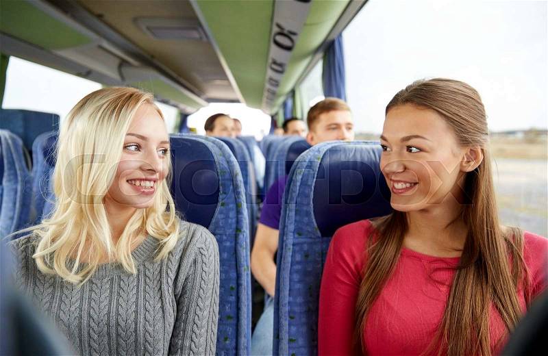 Transport, tourism, friendship, road trip and people concept - happy young women sitting and talking in travel bus, stock photo