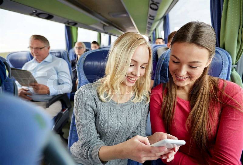 Transport, tourism, road trip and people concept - happy young women or friends in travel bus texting or reading message on smartphone, stock photo
