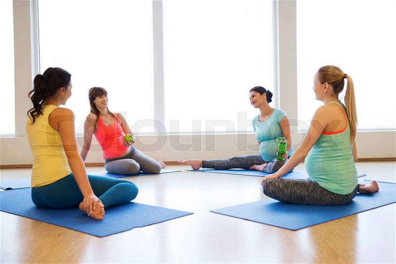 Pregnancy, sport, fitness, people and healthy lifestyle concept - group of happy pregnant women with water bottles sitting on mats and talking in gym, stock photo