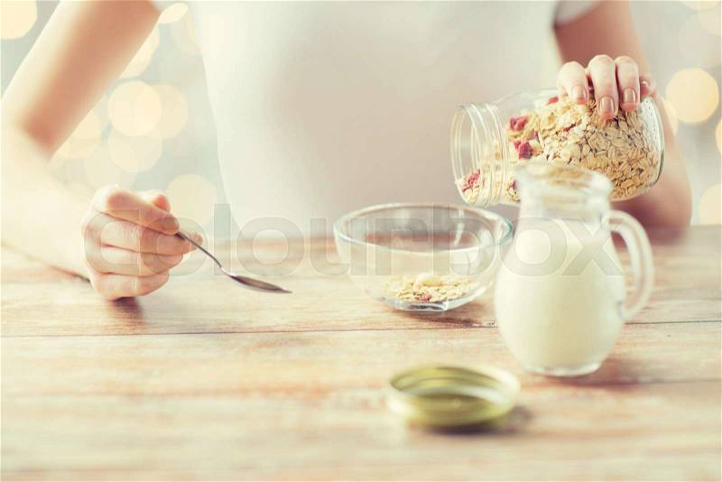 Food, healthy eating, people and diet concept - close up of woman eating muesli with milk for breakfast over holidays lights background, stock photo