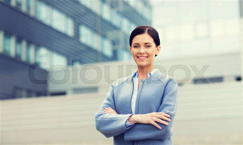 Business and people concept - young smiling businesswoman over office building, stock photo