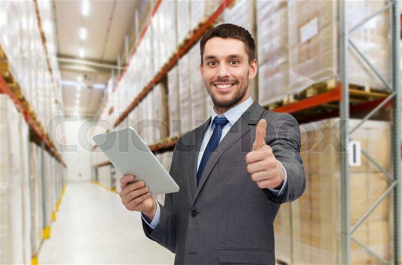 Wholesale, logistic business, export, technology and people concept - smiling businessman with tablet pc computer showing thumbs up over warehouse background, stock photo