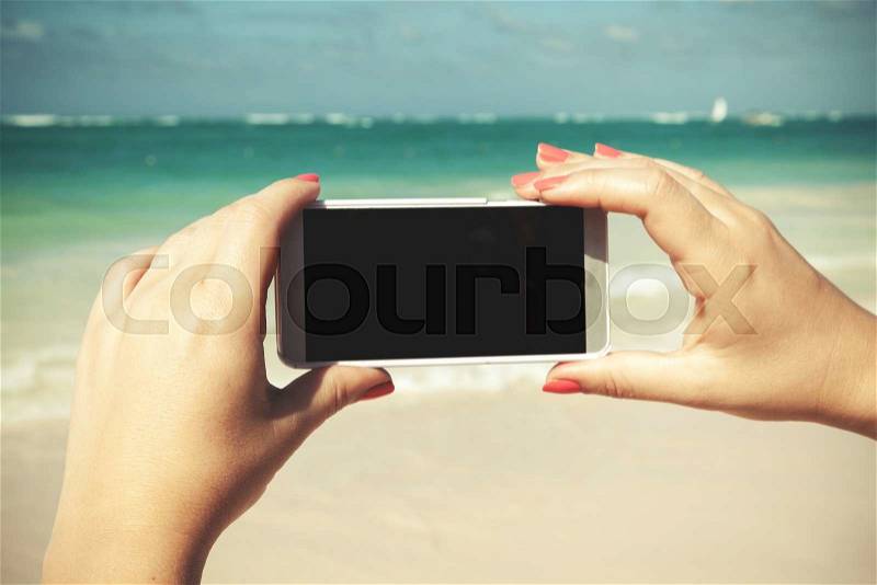 Woman holds smart phone in hands for taking outdoor photo on a summer beach in Dominican republic. Vintage tonal correction photo filter, old style effect, stock photo