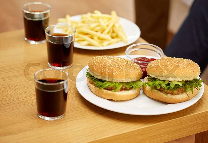 Fast food, unhealthy eating and junk-food concept - close up of hamburgers, drinks and french fries on table at home, stock photo