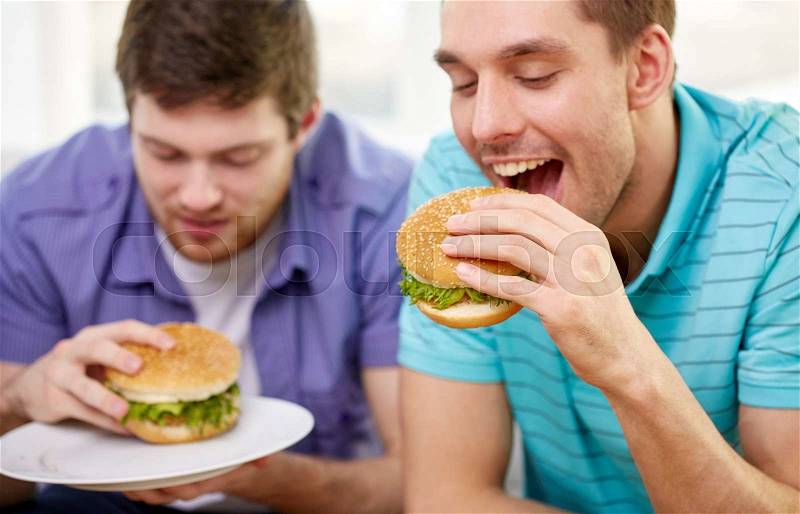 Fast food, unhealthy eating, people and junk-food - close up of happy friends eating hamburgers at home, stock photo