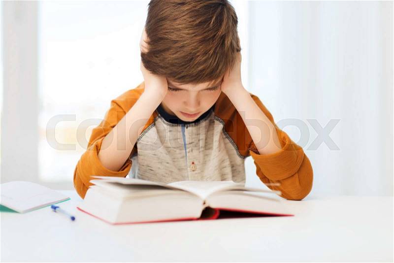 Education, childhood, people, homework and school concept - bored or displeased student boy reading book or textbook at home, stock photo