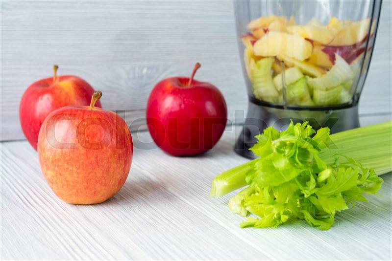 Apples, a bunch of celery, and a food processor on white table. Concept of healthy nutrition, stock photo