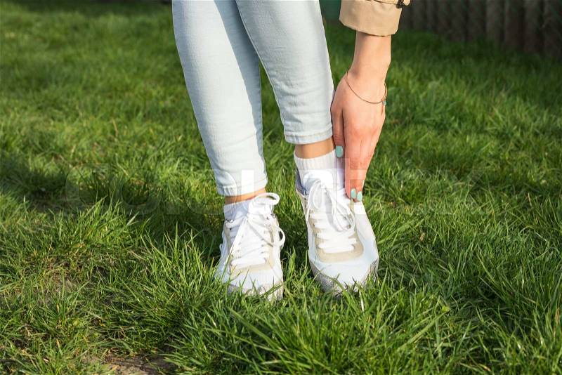 Slender female legs in jeans and white sneakers on a green lawn on a sunny day, stock photo