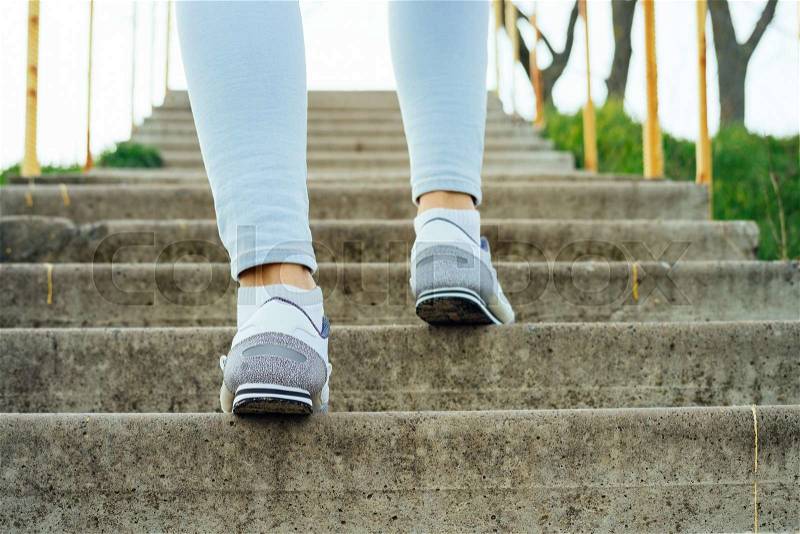 Female legs in jeans and sneakers, climb the concrete stairs outdoors, stock photo