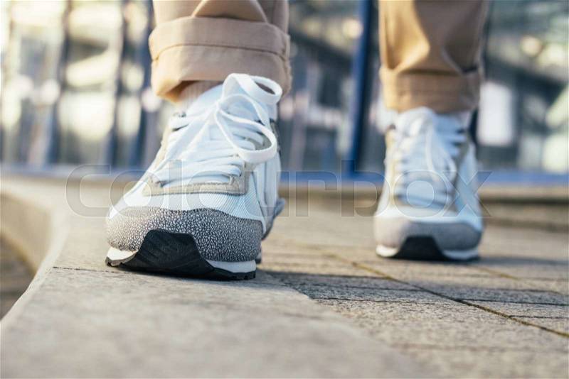 Legs in beige pants and white sneakers are on the sidewalk. Close-up, low angle shooting, shallow depth of field, stock photo