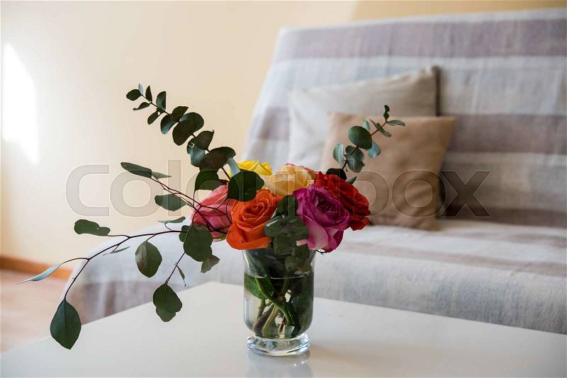 Summer light home interior with sofa and pillows on a background, colorful roses in the vase, stock photo