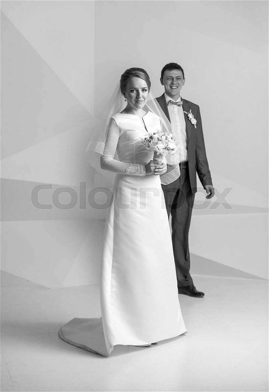 Black and white shot of happy bride with bouquet posing at studio, stock photo