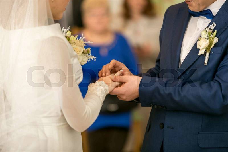 Closeup of young groom putting wedding ring on bride\'s finger, stock photo