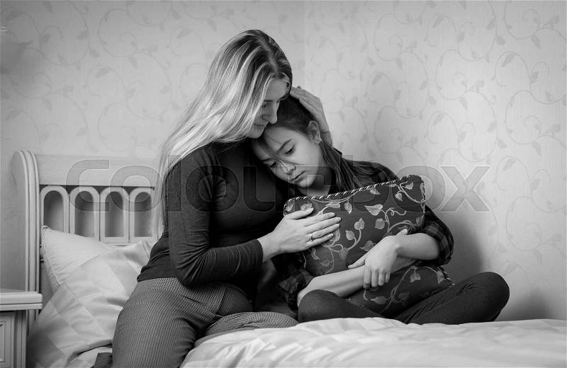 Black and white portrait of young mother consoling teenage daughter on bed, stock photo