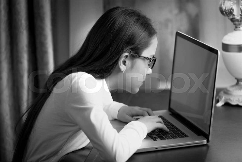 Closeup black and white portrait of teen girl with bad sight typing message on laptop, stock photo