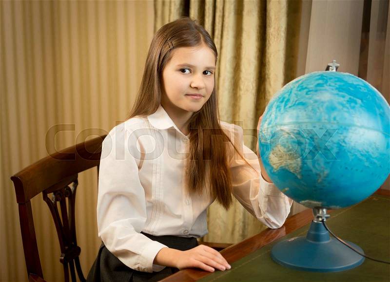 Portrait of beautiful schoolgirl posing at cabinet with Earth globe, stock photo
