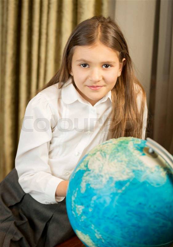 Beautiful smiling schoolgirl posing with Earth globe at cabinet, stock photo
