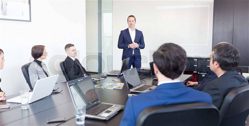 Successful team leader and business owner leading informal in-house business meeting. Businessman working on laptop in foreground. Business and entrepreneurship concept, stock photo