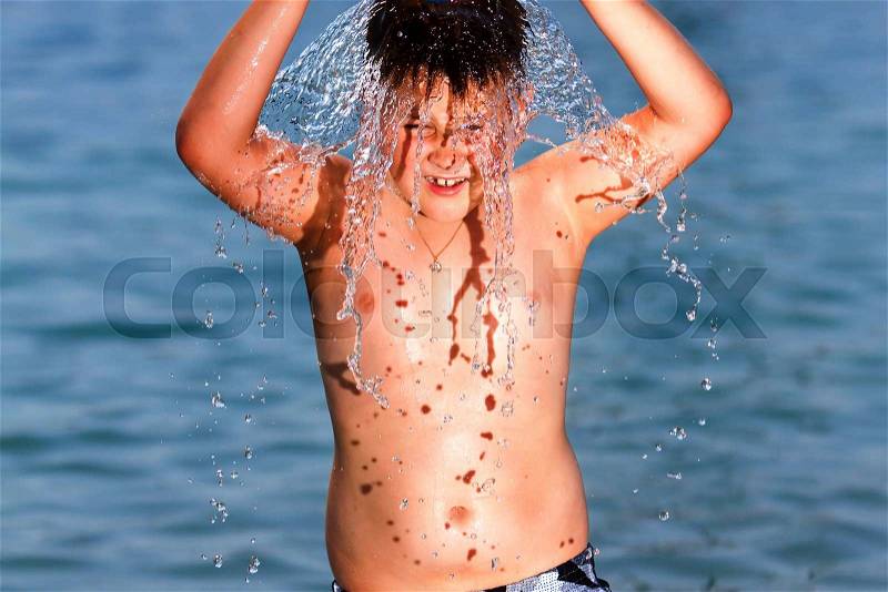 Boy splashing water on his head by the sea, stock photo
