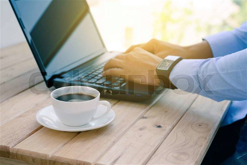 Coffee cup with closeup man typing a laptop on wooden table, stock photo