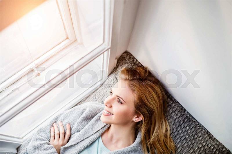 Beautiful blond woman lying on window sill smiling, looking out of window, stock photo
