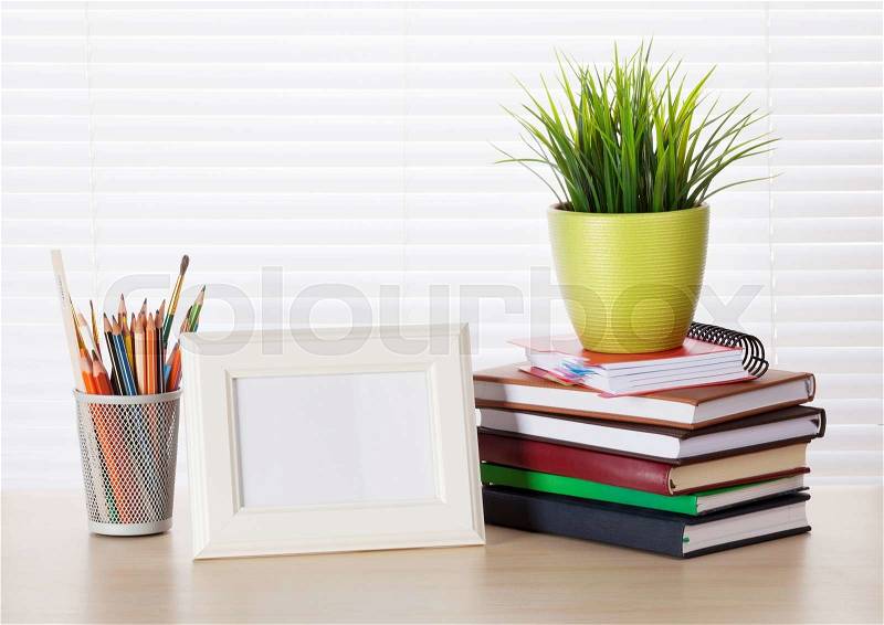 Office workplace with photo frame, books and pencils on wood desk table in front of window with blinds, stock photo