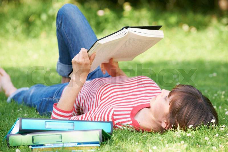 Female Student Reading Textbook In Park, stock photo