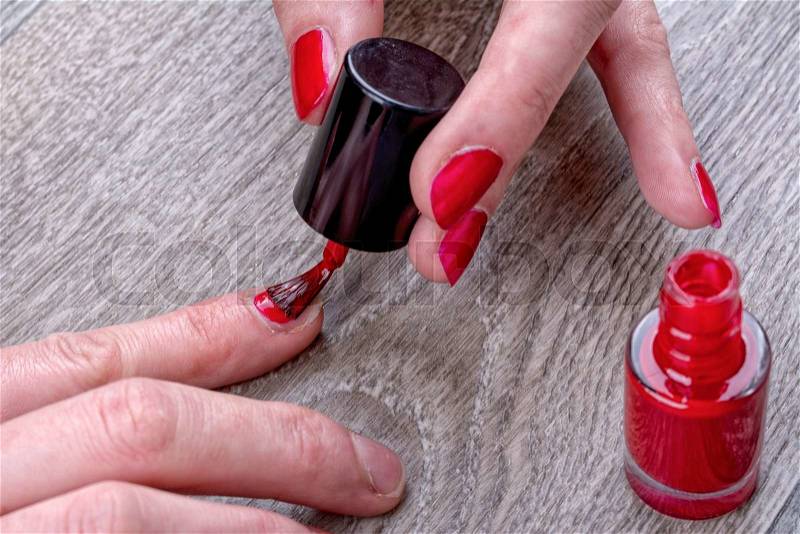 Close-up of female hands painting red nail varnish, stock photo
