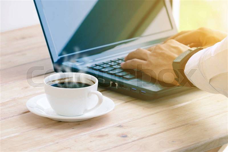 Coffee cup with closeup man typing a laptop on wooden table, stock photo