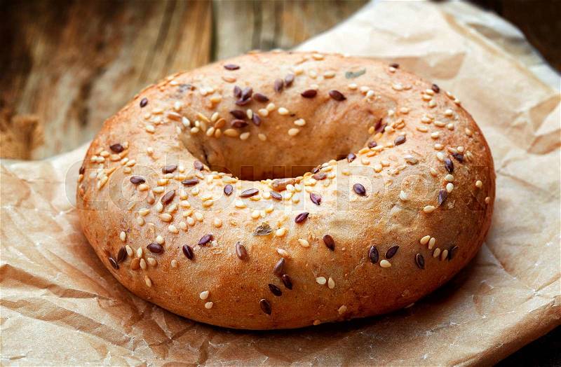 Fullgrain bagel with seeds in paper bag on wooden table, stock photo