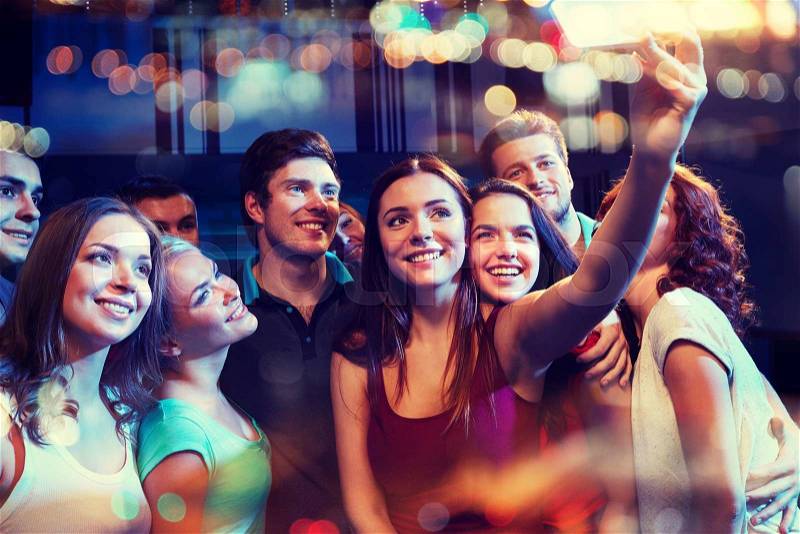Party, technology, nightlife and people concept - smiling friends with smartphone taking selfie in club, stock photo